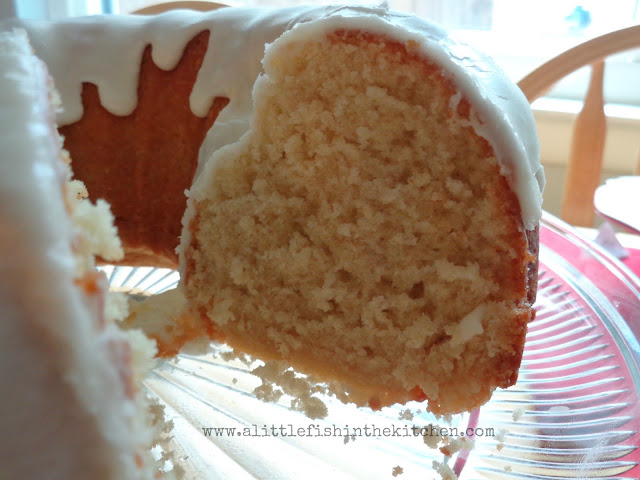 An old-fashioned buttermilk pound cake is on a clear glass baking dish The cake is cut revealing a tender, golden crumb underneath a thich, rich white glaze.