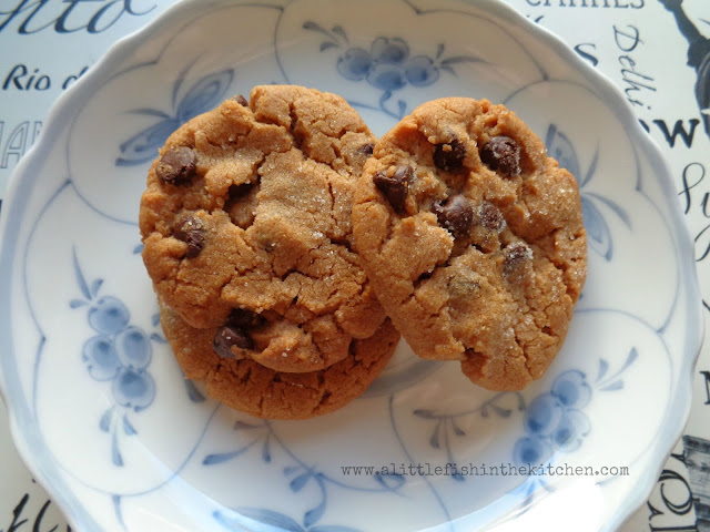 Four tempting peanut butter chocolate chip cookies are stacked on a white ceramic plate with a vintage blue floral pattern. The cookies have perfectly crackled tops and sweet chocolate chips are visible in the tops of each cookies.