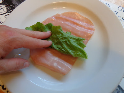 Two layers of thinly sliced lunch meat, ham and salami are being topped with small strips of Romain lettuce. 