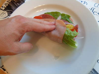 A hand is demonstrating how to tuck and roll up the layers of ingredients to make easy low carb Italian roll ups. 