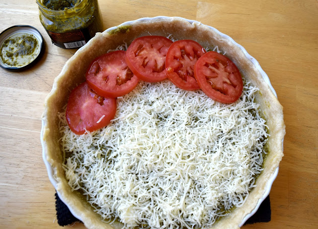 A layer of shredded Italian cheeses and tomatoes are placed into the pesto-coated parbaked pie crust.
