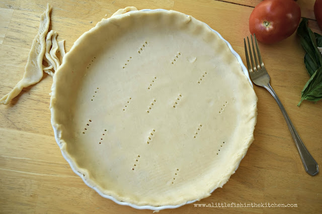 A prepared pie crust is formed into a white ceramic tart dish, a fork is used to prick small holes into the uncooked pie crust to help prevent lifing.