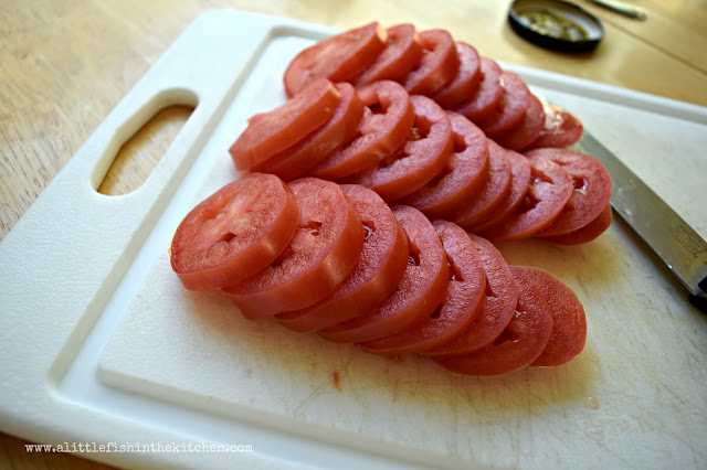 three beautiful rows of sliced fresh Roma tomatoes are layed out on a white plastic cutting board.