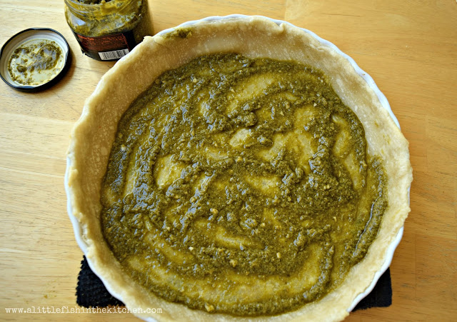 A layer of bright green prepared pesto covers the bottom of a parbaked pie crust.