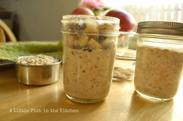 A mason jar is half way filled with creamy, prepared overnight oats. A generous portion of fresh topping, chopped apple, chopped pecan and raisins are resting on top, ready to enjoy.