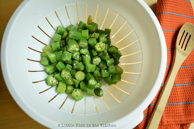 Beautifully green, fresh sliced okra is in a white colander. It's  ready to be breaded and fried. 