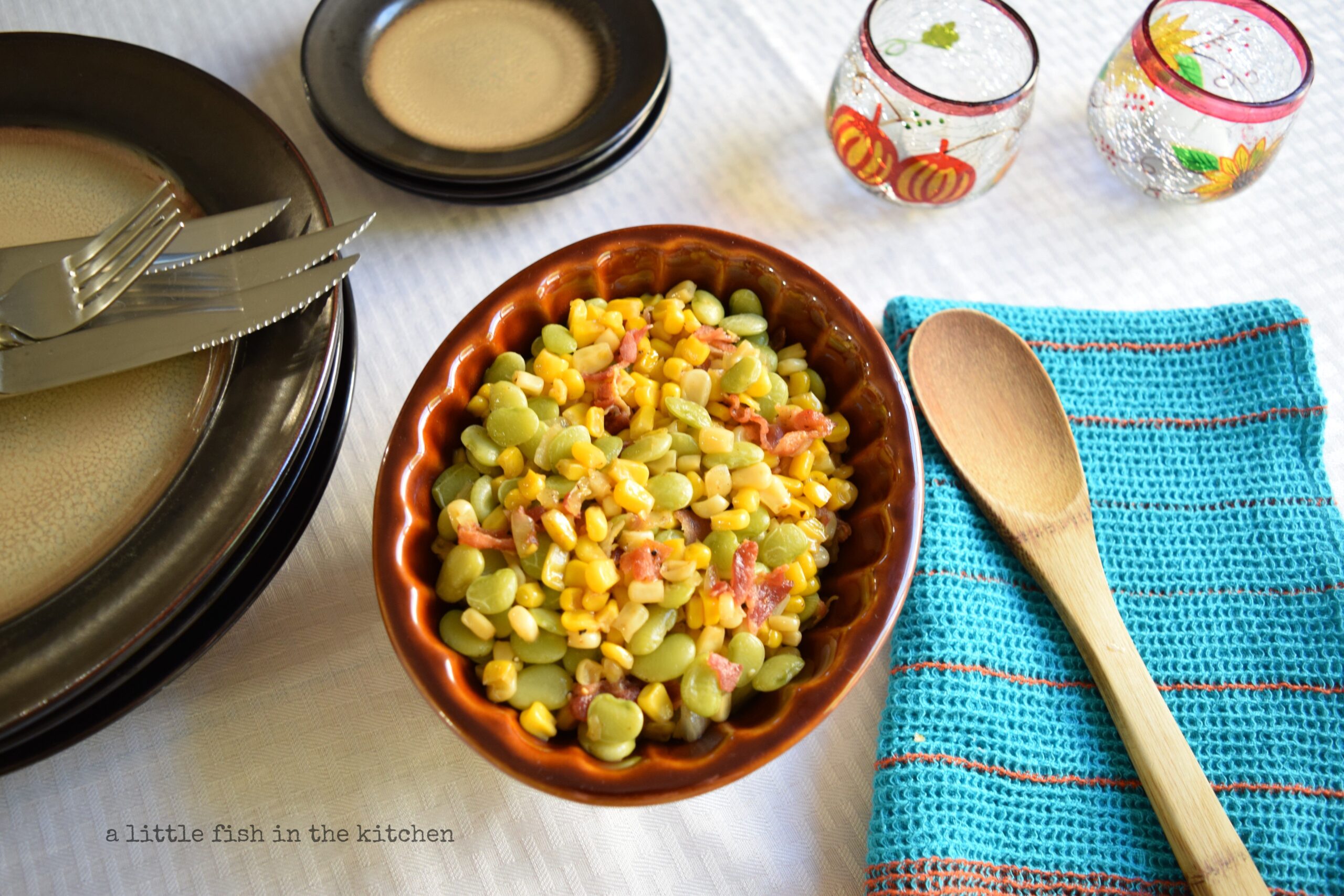 Colorful succotash with bacon is served in a brown ceramic dish with lovely scalloped edges. Golden yellow corn kernels, green Lima beans, and warmly colored bacon bits looked deliciously festive and delicious on the plate. 