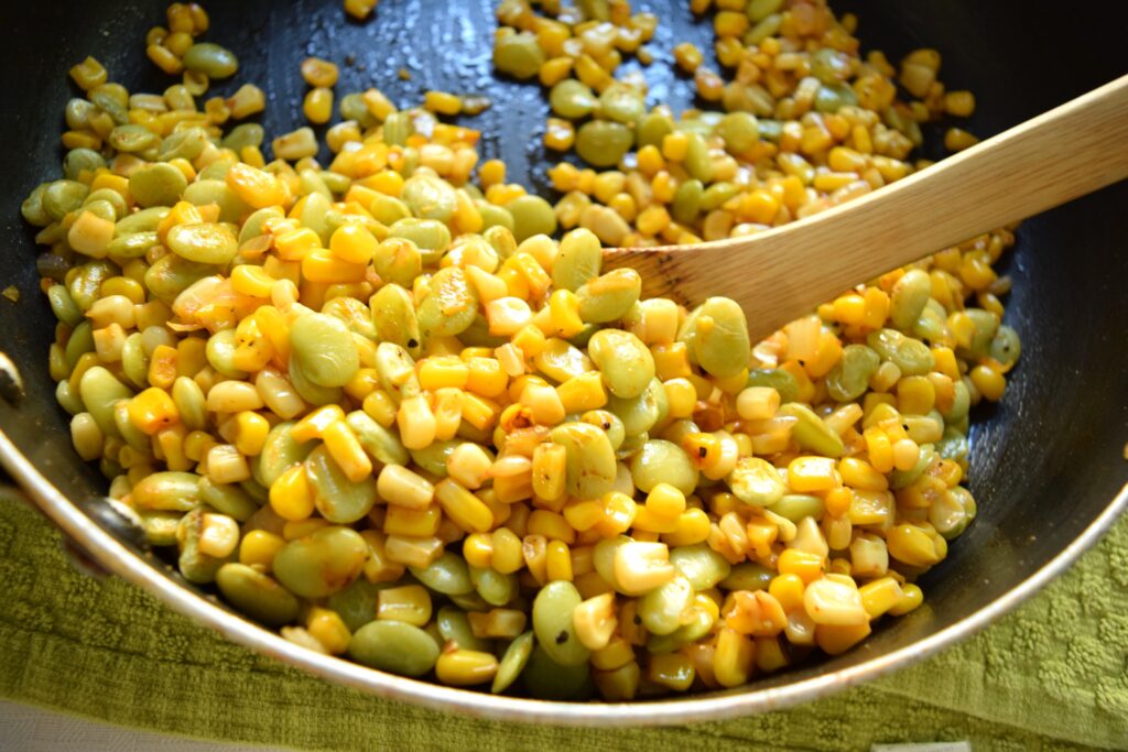 Golden yellow corn kernels and spring green lima beans are sauteed in a skillet. Speckled bits of pepper and smoked paprika are visible on the veggie medley.