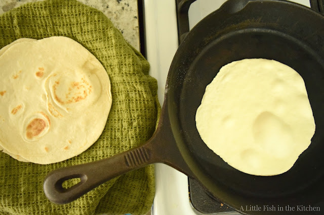 Freshly cooked, hot tortillas are transferred to a plate as they are removed from the cast iron skillet with tongs. 