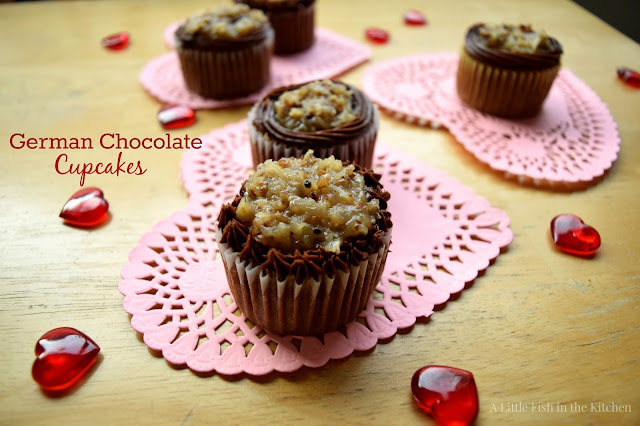 Rich German chocolate cupcakes are ready to enjoy. They are festively displayed on a table with pink heart-shaped paper doilies and shiny glass hearts scattered around.