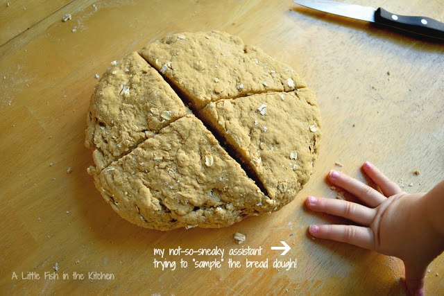 The warm brown soda bread dough is shaped into a disk and scored with a large X shape on top for baking. 