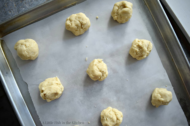 Generous tablespoons of lemon cookie dough are spaced out on a metal baking sheet lined with parchment paper. They ready for the oven. 