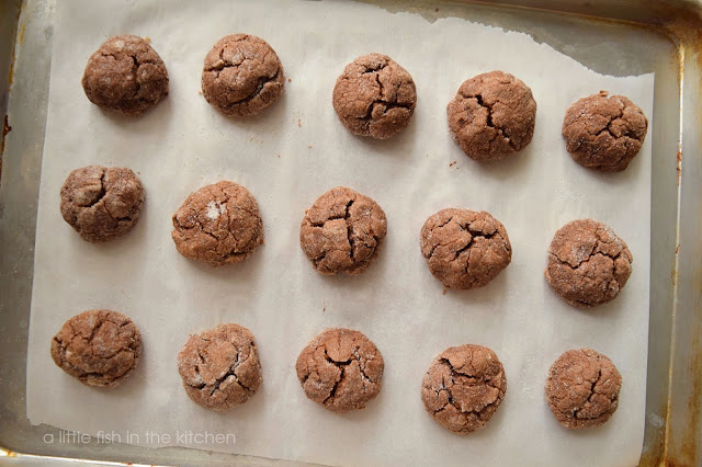Fifteen petite cappuccino crinkles are fresh baked, still on the pan and cooling on a rack. The cholate cookies have crinkled tops and a crisp  