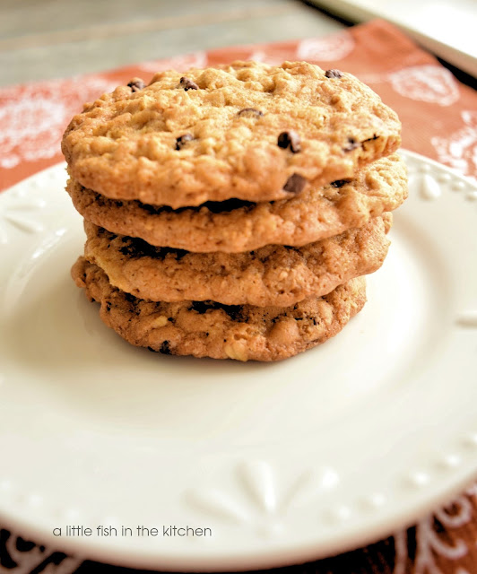 Tender oatmeal chocolate chip cookies are stacked on a small white dessert plate. The cookies are somewhat thin and look light and soft. They are perfectly golden and studded with bits of oats and chocolate chips.
