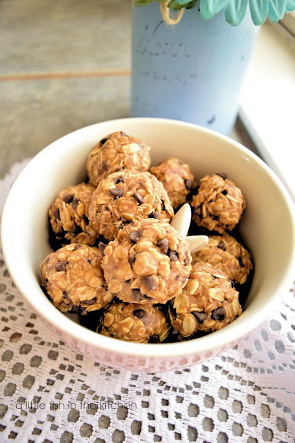 A fresh batch of oat, maple energy bites is ready to enjoy. Hearty oats, sweet chocolate chips and peanut butter are all visible in these no-bake cookies. The energy bites are in a pink ceramic bowl with a white ceraminc bunny in the center. Beside the bowl is a large mason jar that's painted sky blue with pastel  flowers in it.