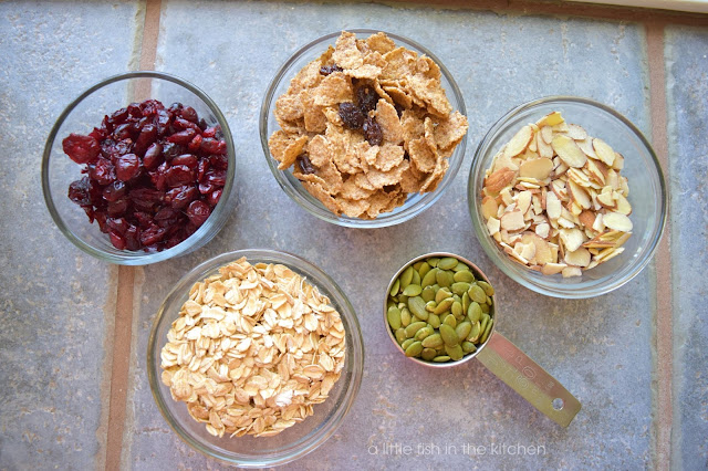The ingredients to make a batch of homemade pan toasted cranberry almond muesli are gathered in small clear glass ramekins: slivered almonds, pepitas, raisin bran cereal, quick cooking oats and dried cranberries are portioned out and ready to use for this recipe. 