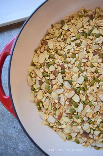 Slived almonds, pepitas, and whole oats have freshly pan toasted and cooling in side of a red coated cast iron skillet. 