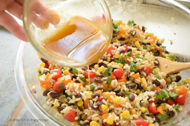 Vibrantly Mexican-style brown rice salad is chockful of diced fresh peppers, corn kernel, black beans, cherry tomatoes, fluffy brown rice and fresh cilantro. The zesty honey lime vinaigrette is poured over the colorful, prepared rice salad in it's preparation. 