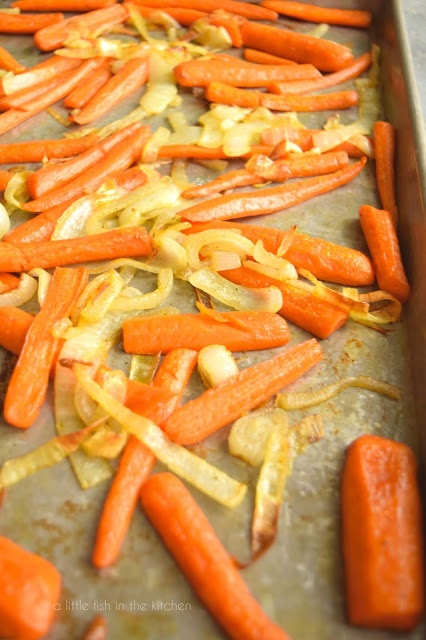Tender, freshly roasted carrots and onions rest on a metal cooking sheet.