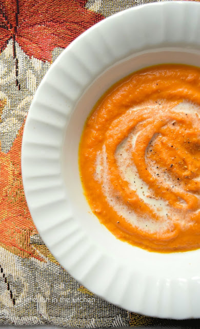 A single serving of vibrantly colored amber soup is in a white ceramic bowl, ready to eat. The soup is eye-catchingly garnishes with small splash of cream and freshly cracked black pepper.