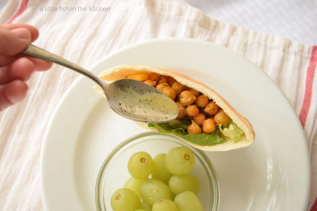 A hearty pita pocket stuffed with crisp green salad and crunch roasted chickpea is drizzled with a delicious homemade vinaigrette before serving.