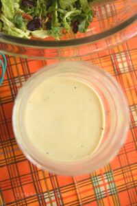 Flavorful, creamy apple cider vinegar salad dressing is featured in a clear mason jar.  It's warm ivory color and small flecks of zesty ground black pepper are visible.  