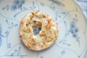 A single apple slice topped with flavored cream cheese and chopped pecans sits on a white plate with a light blue decorative floral pattern.