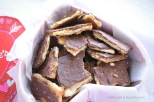 Layers of crisp saltine cracker, homemade caramel and chocolate are featured in this close-up shot of homemade cracker candy. The sweet and salty layers of this homemade candy are inviting. The unevenly broken pieces of candy give this chocolate treat a rustic appearance, but they are set inside a paper-lined, heart-shaped treat box. It's a sweet presentation for a festive Valentine's day gift! 