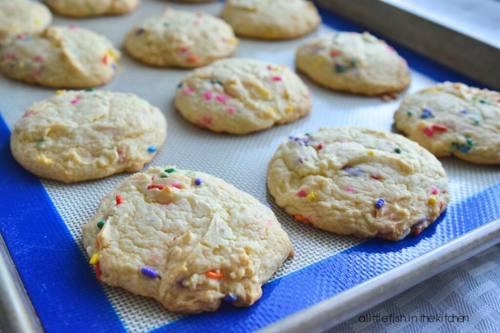 freshly baked vanilla cake mix cookies with sprinkles are cooling on a rack. The soft cake mix cookies with colorful sprinkles mixed in look inviting. 