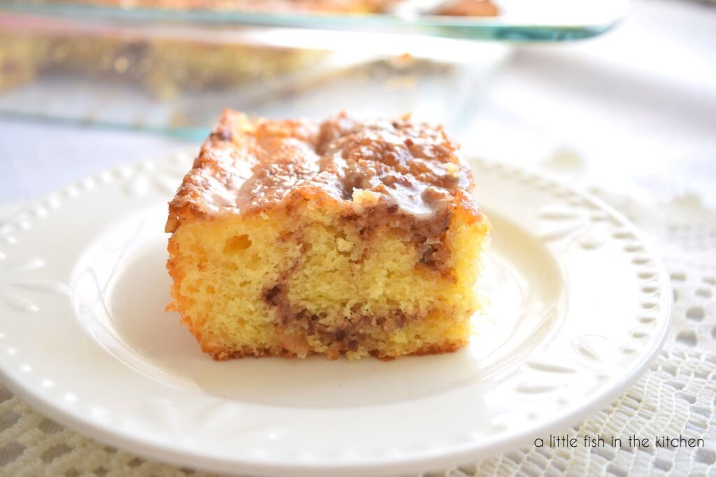 A square slice of moist yellow cake is shown from the side. An inviting swirl of cinnamon and sugar is clearly visible in this slice of honey bun cake.