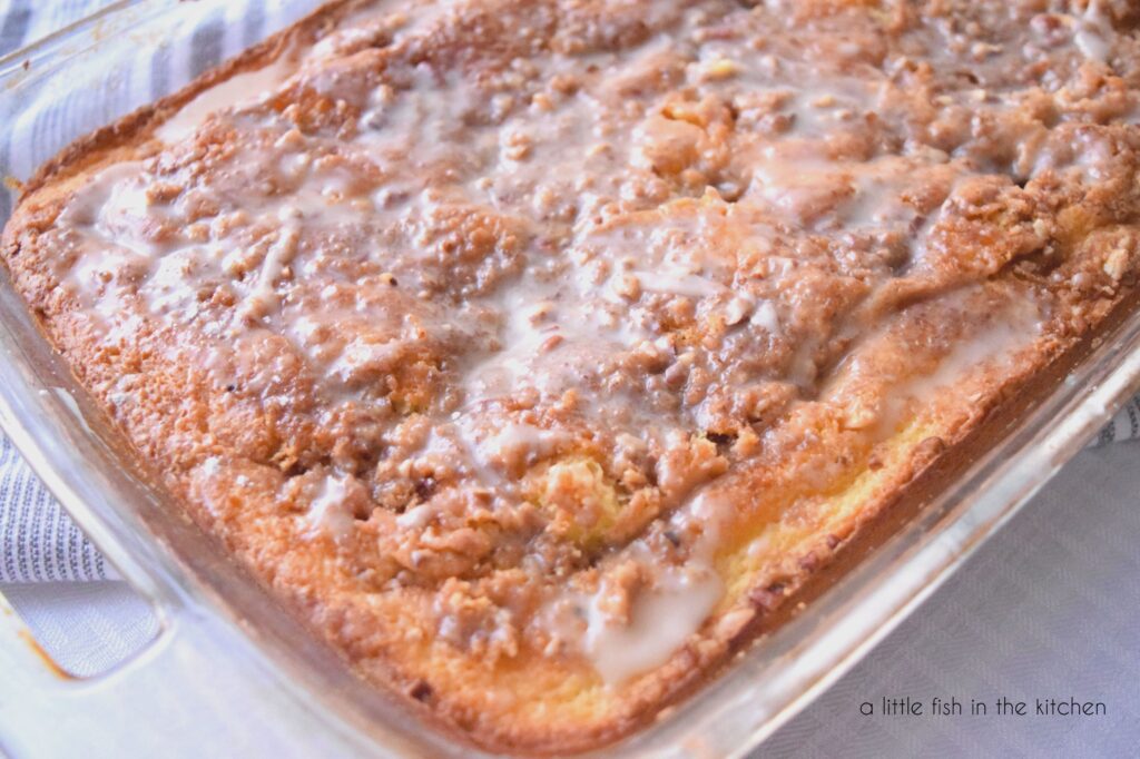 Bit of cinnamon streusel are visible on top of the warm cake. A tempting ivory-colored glaze is drizzled over the top.