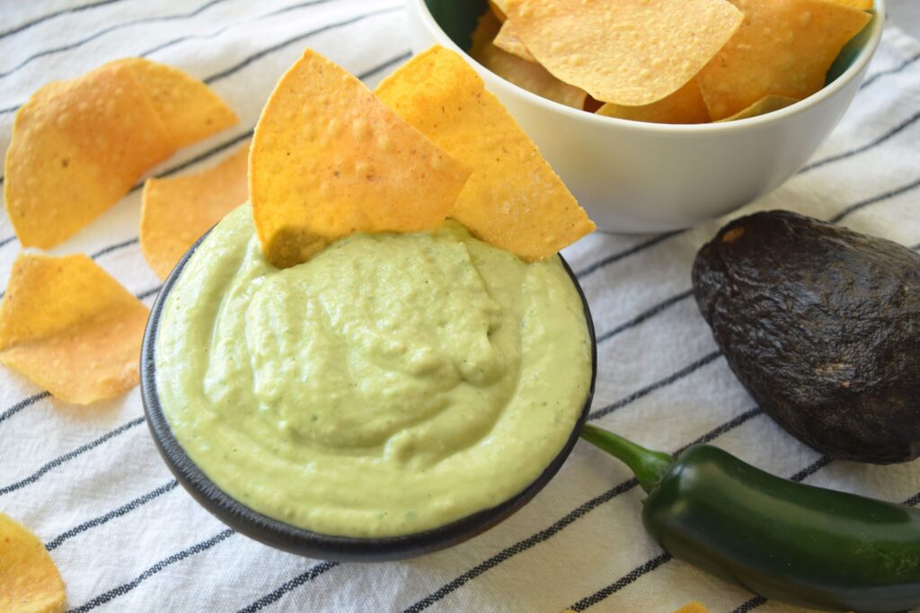 Creamy Avocado Salsa in a small black serving bowl with tortilla chips