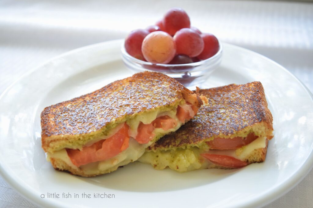 sliced tomato-pesto grilled cheese with grapes on a plate. 