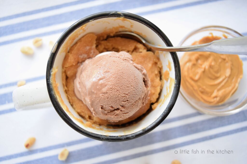 A mug cake sits on a blue and white table runner. It's topped with a melting scoop of chocolate ice cream. 