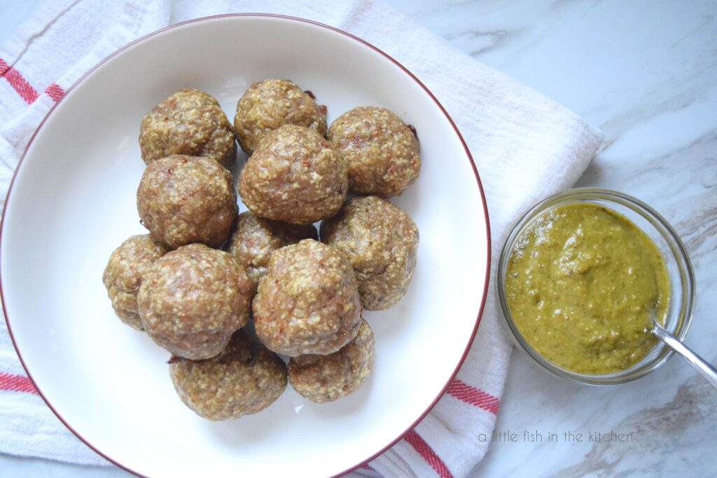 Meatballs are in a white bowl with a small bowl of pesto on the side. 