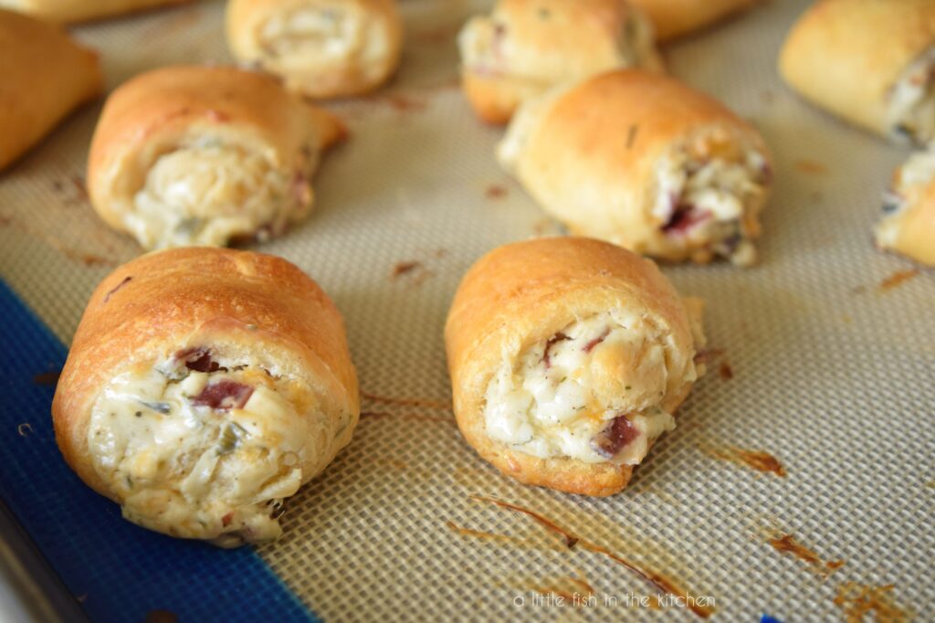 Close-up picture of two roll ups on a baking sheet. The pastry is golden brown and the filling is white with bits of herbs, bacon and cheese mixed in. 