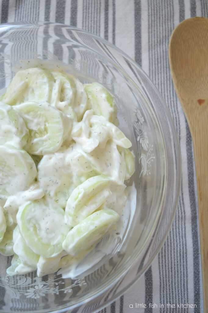 Slices of fresh cucumber are coasted in white sour cream and specks of green dill are visible in the creamy sauce. 