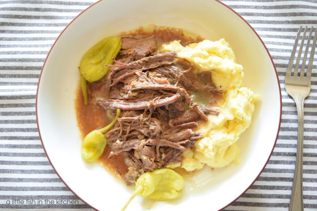 Close up of a bowl filled with Mississippi pot roast on a bed of mashed potatoes. 