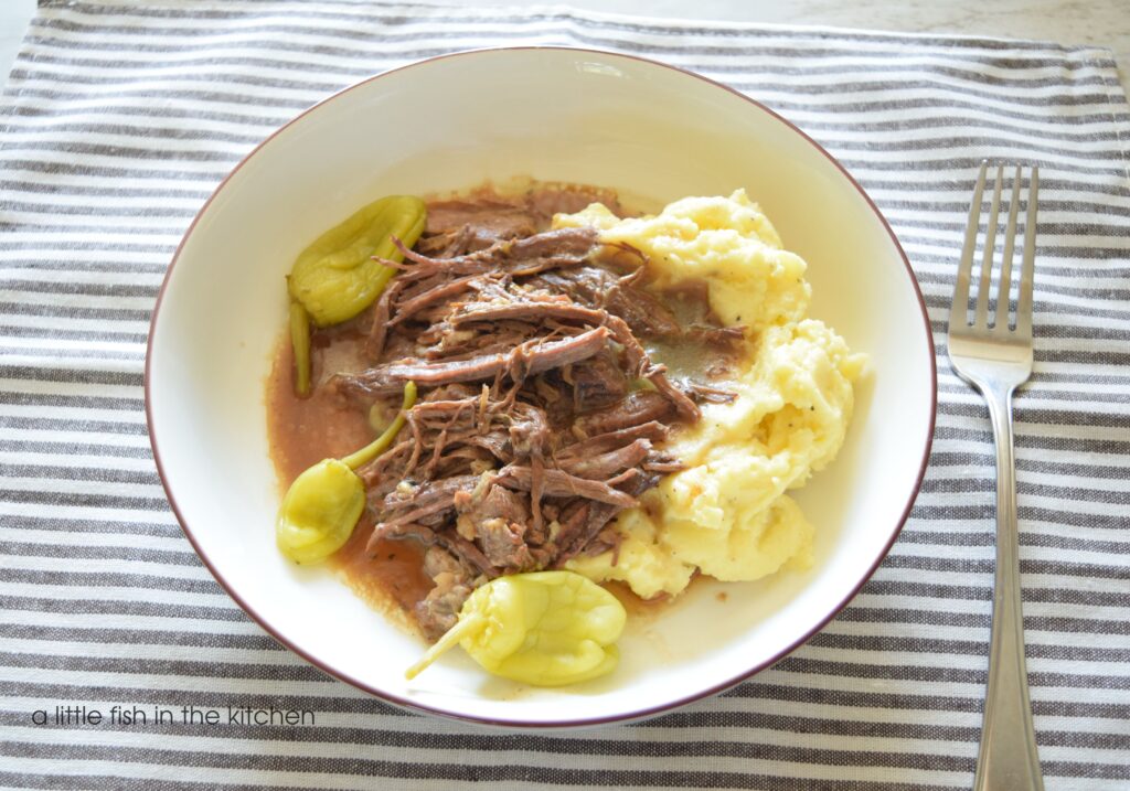 A white bowl filled with shredded Mississippi pot roast on a bed of mashed potatoes 