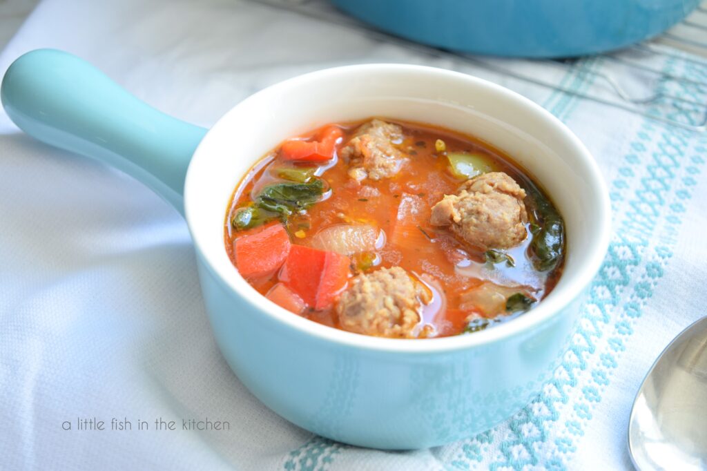 Sausage and pepper soup in a light blue soup bowl with a spoon beside the bowl. 