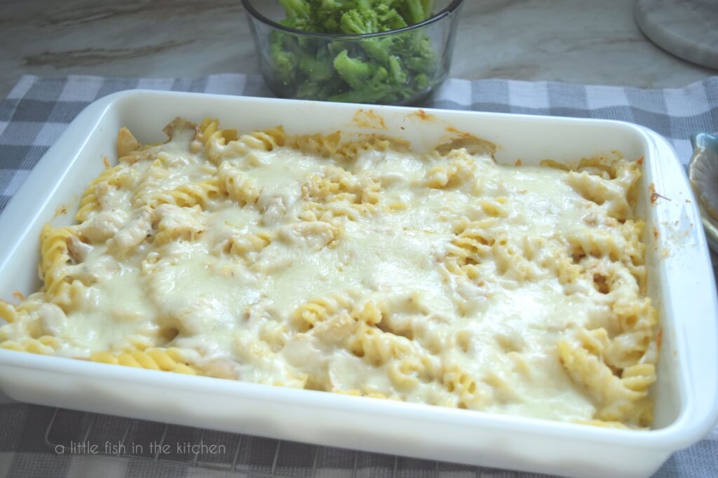 Easy Chicken Alfredo Bake is in a white casserole dish with bowl of steamed broccoli beside it. 