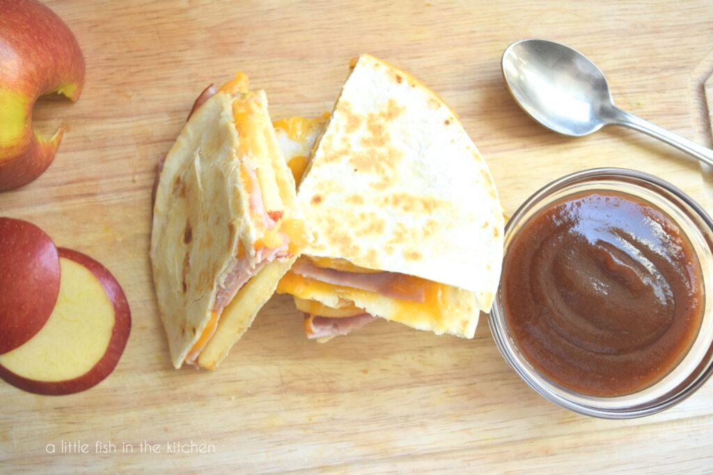 This pictures shows the top of a stack of quesadilla slices and small bowl of apple butter next to it. 