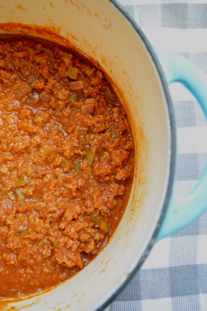 A teal-colored dutch oven is shown filled with warm pumpkin chili.  