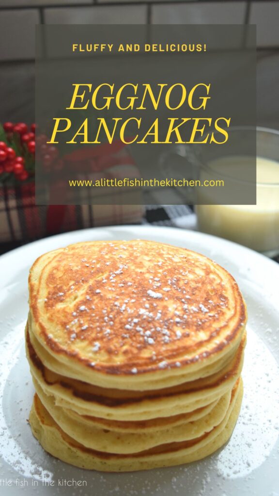 Pin image for this recipe. The recipe title and name of this blog are written in a gold font on top of a dark teal overlay. The picture is of a stack of four pancakes on a white plate sitting on top of a black and white tea towel. A clear mug filled with egg nog and a decorative wrapped holiday gift are slightly blurred in the background.