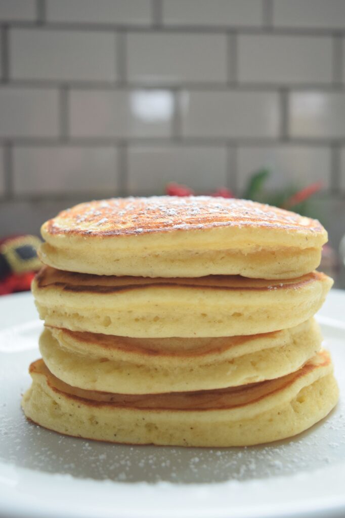 A close up shot from the side of a stack of four eggnog pancakes siting a on white plate.