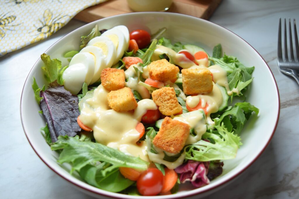 A white bowl with a green salad inside is drizzled with golden, homemade honey mustard salad dressing. 
