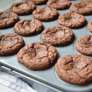 A mini muffin pan filled with tempting chocolate brownies is cooling on a rack. The delightfully crackled tops on the brownie bites make them irresistible.