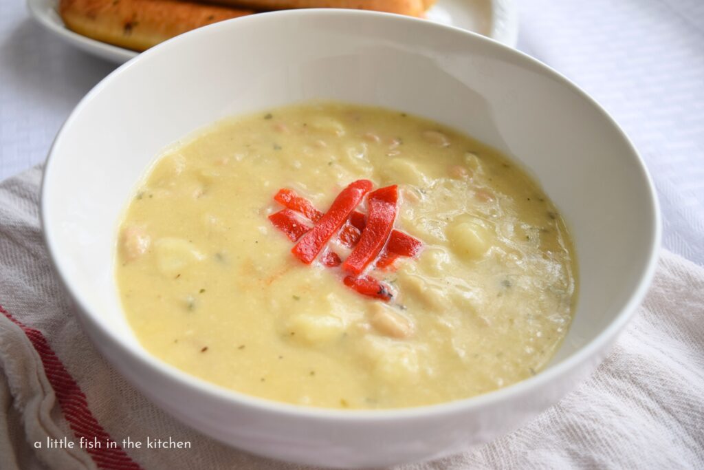 Creamy Potato and Bean chowder is in a white bowl and garnished with strips of bright red roasted red pepper.