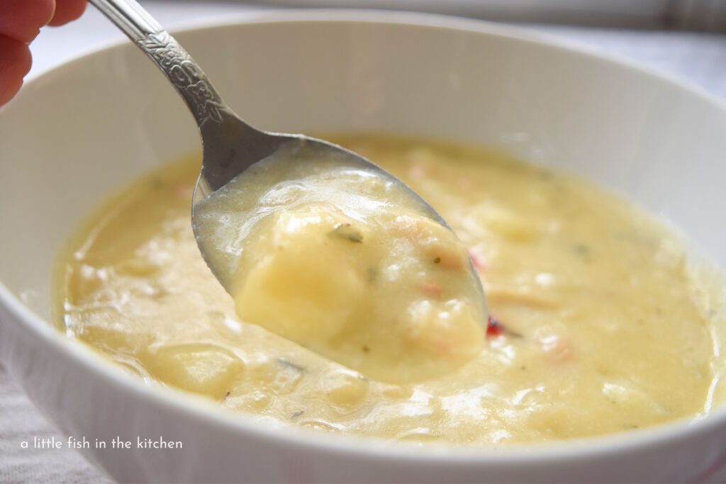 Bits of potato, herbs and red pepper are visible in a spoonful of potato and bean chowder, 