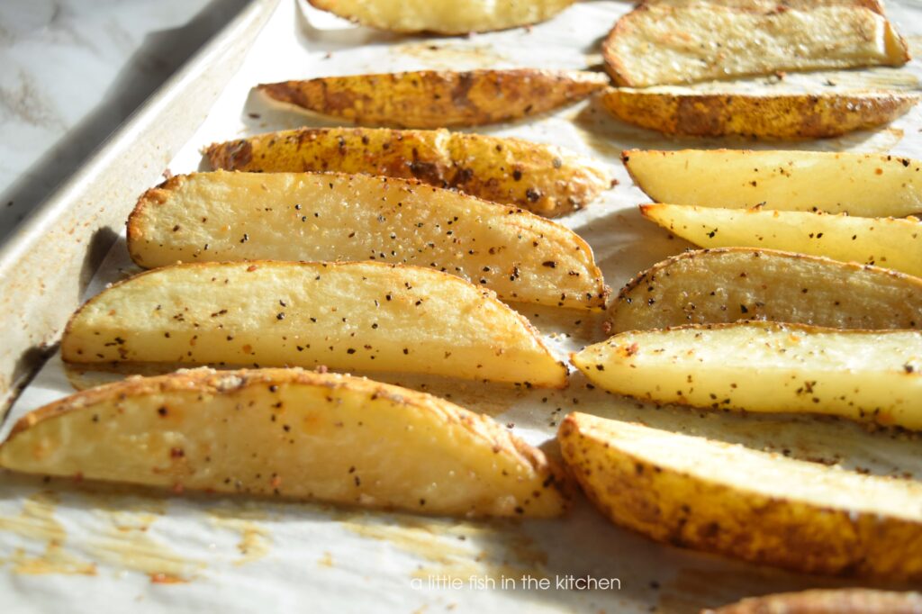 Pigskin Potatoes are fresh out of the oven, golden brown and crisp. Bits of fresh ground pepper, and minced garlic are visible on the seasoned potato wedges. 